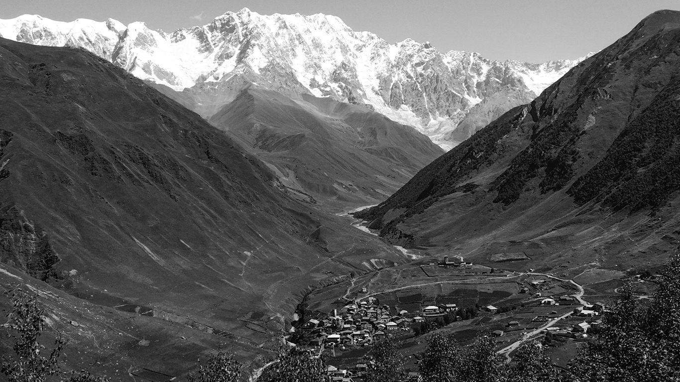 Der Blick auf Ushgulis mit dem Schchara-Gletscher im Hintergrund zeigt die Ortsteile Chibiani (Zhibiani) und Chwibiani (Schwibiani). Oberhalb der Dorfgemeinschaft ist das Kloster Lamaria zu sehen, eines der wichtigsten Einsiedel-Kloster des georgisch-orthodoxen Christentums.